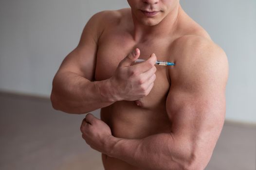 A muscular man with a naked torso holds a dope syringe. Unrecognizable bodybuilder puts himself steroids. Athlete cheats for gaining muscle mass