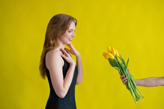 Caucasian woman accepts tulips as a gift on yellow background