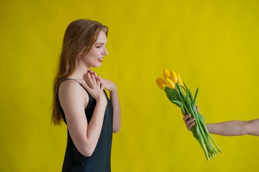 Caucasian woman accepts tulips as a gift on yellow background