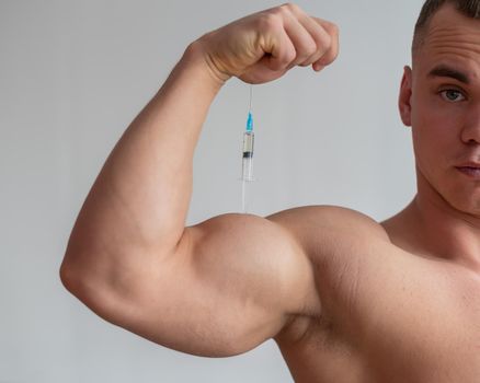 Muscular male bodybuilder with a naked torso holds a dope syringe. The athlete puts himself an injection of growth hormone. Prohibited anabolics