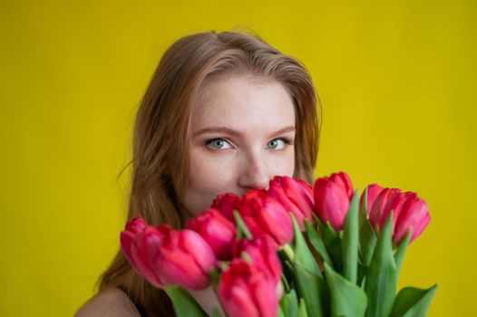 Woman with a bouquet of red tulips on a yellow background. Happy girl in a black dress holds an armful of flowers. Gift for Valentine's Day. The most romantic day of the year