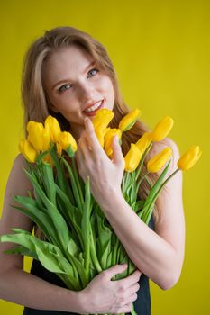 Caucasian woman with an armful of yellow tulips on a yellow background. International Women's Day. Bouquet of spring flowers.