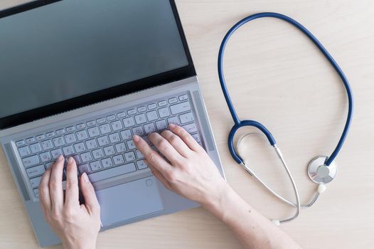 Top view of hands on the keyboard. Woman doctor at the desk typing on a laptop. A nurse fills out a patients electronic card