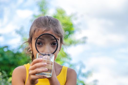 The child examines a glass of water with a magnifying glass. Selective focus. Kid.