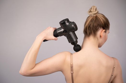 Caucasian woman giving herself a back massage with a gun
