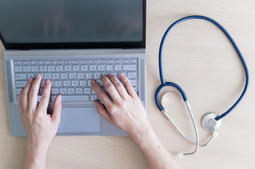 Top view of hands on the keyboard. Woman doctor at the desk typing on a laptop. A nurse fills out a patients electronic card