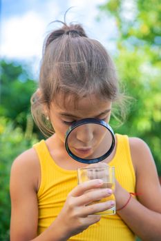 The child examines a glass of water with a magnifying glass. Selective focus. Kid.