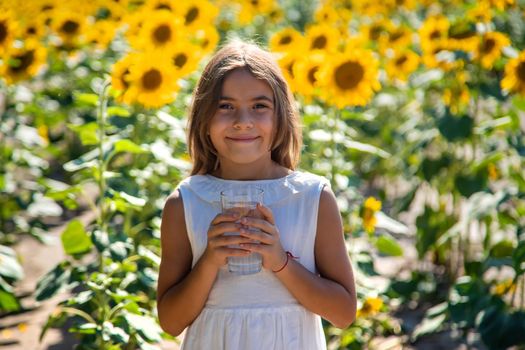 The child drinks water from a glass in a field of flowers. Selective focus. Kid.