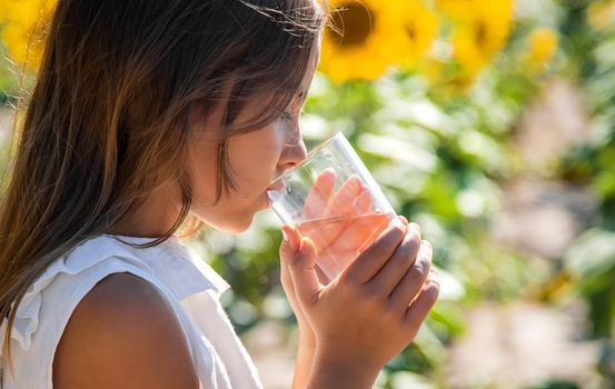 The child drinks water from a glass in a field of flowers. Selective focus. Kid.