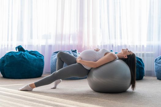 Beautiful european woman doing pregnant exercises. Expectant mother is doing exercises with a fitness sword. Yoga for expectant mothers