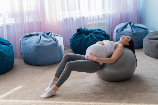 Beautiful european woman doing pregnant exercises. Expectant mother is doing exercises with a fitness sword. Yoga for expectant mothers