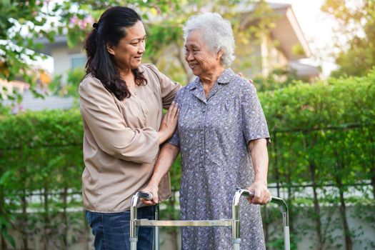 Caregiver help Asian elderly woman disability patient walk with walker in park, medical concept.