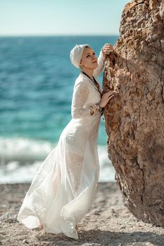 Middle aged woman looks good with blond hair, boho style in white long dress on the beach decorations on her neck and arms