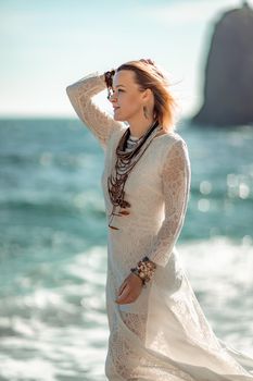 Middle aged woman looks good with blond hair, boho style in white long dress on the beach decorations on her neck and arms