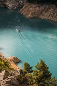 Boat floating and leaving a trail on the turquoise water surface. Summer vacation holidays. Congost de Mont Rebei, Catalonia, Spain.