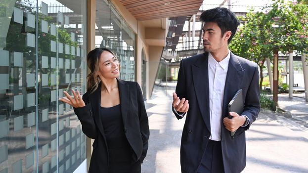 Two happy business colleagues talking to each other while walking outside modern office building.