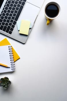 Simple workplace with laptop computer, coffee cup, notebook and sticky note on white table.