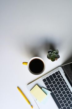 Simple workplace with computer laptop, coffee cup, notebook and succulent plant on white table.