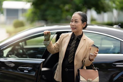 Portrait of Asian Senior Business woman step out luxury car while come to office. Account and Finance concept