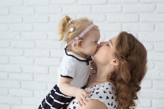 Mother helps her deaf baby daughter putting hearing aid in little girl's ear indoors - cochlear implant and innovative medical technologies