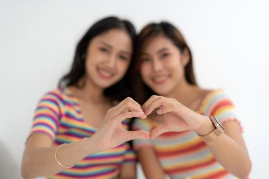 Asian affectionate feelings lesbians couple ladies romantic date make fingers heart shape symbol lean heads lovers eyes closed wear casual t-shirts in rainbow.