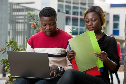 Education concept - Students, girl and boy do their homework using a laptop or documents as research information sitting outside.