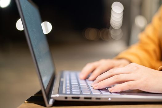 Closeup of female hands on a computer touchpad. Freelancer remotely works on a laptop in the fresh air. A woman is studying on the street in the evening