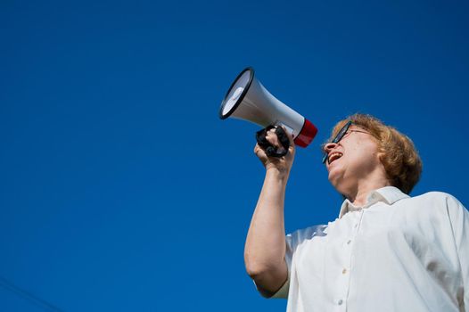 An emotional elderly woman pushes demands into a megaphone. An angry retired woman is fighting for the rights of older people. The female leader of the rally voiced claims to the loudspeaker