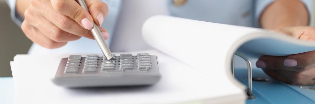 Close-up of woman accountant working on annual report on financial situation in company. Pressing on calculator numbers with silver pen. Banking concept