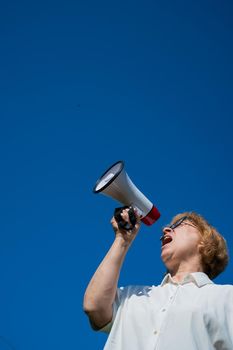 An emotional elderly woman pushes demands into a megaphone. An angry retired woman is fighting for the rights of older people. The female leader of the rally voiced claims to the loudspeaker