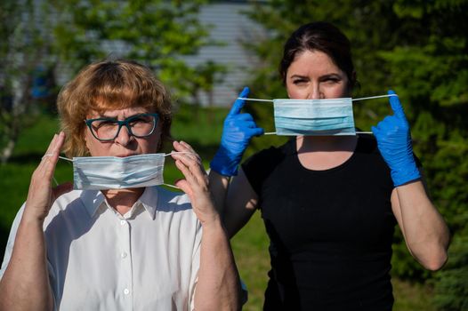 Mom and daughter put on medical masks against the spread of infection. Two elderly and middle-aged women are protected against coronavirus