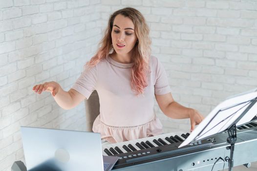 A friendly woman plays the electronic piano and conducts a video blog on her laptop. Stay home. Musical instrument teacher. Distance learning music quarantined