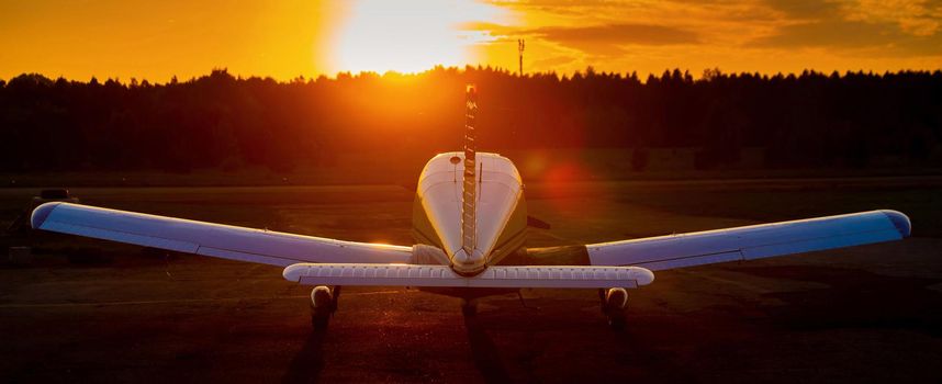 Rear view of a parked small plane on a sunset background. Silhouette of a private airplane landed at dusk