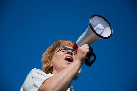 An emotional elderly woman pushes demands into a megaphone. An angry retired woman is fighting for the rights of older people. The female leader of the rally voiced claims to the loudspeaker