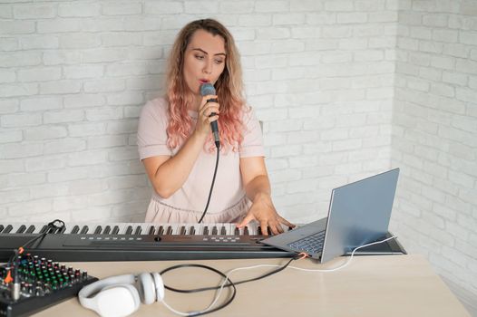 A woman records a vocal lesson using a laptop and accompanying on a keyboard while at home. The teacher sings a song into the microphone and plays the electronic piano. A blogger is recording a video
