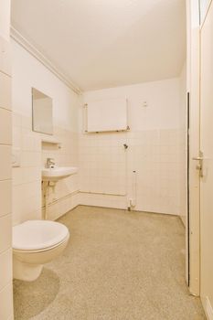 Modern flush toilet and ceramic sink installed on white tiled walls near mirror and towel in small restroom at home