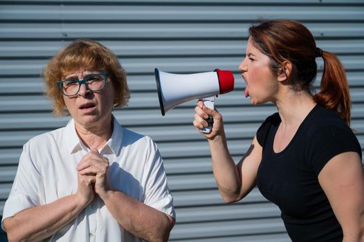 The conflict of generations. An angry middle-aged woman yells at an elderly mother through a megaphone. An adult daughter screams at an unhappy pensioner over a loudspeaker. Quarrel in the family