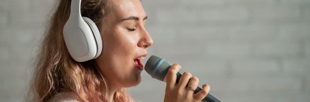 Close-up portrait of a caucasian woman with curly hair singing into a microphone. Beautiful sensual girl in white headphones sings a song in home karaoke
