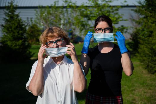 Mom and daughter put on medical masks against the spread of infection. Two elderly and middle-aged women are protected against coronavirus