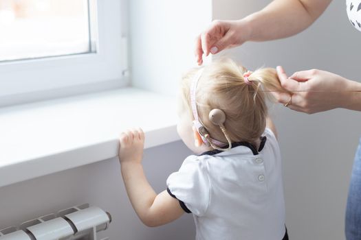 Mother fixing her daughter's cochlear implant hearing aid - deafness and diversity concept. Innovative technologies in treatment deafness