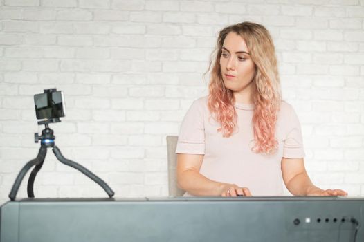 A woman plays the electronic piano and conducts a video blog on a smartphone. A girl takes video from a phone on a tripod. Female music teacher works remotely