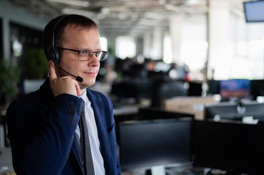 A friendly man from a call center answers a customer with a hands-free headset. Male helpdesk operator talking on the phone. Manager in open space office