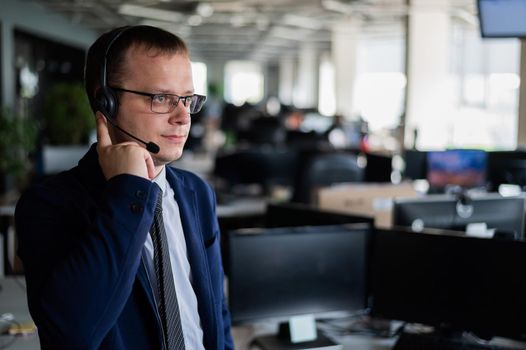 A friendly man from a call center answers a customer with a hands-free headset. Male helpdesk operator talking on the phone. Manager in open space office