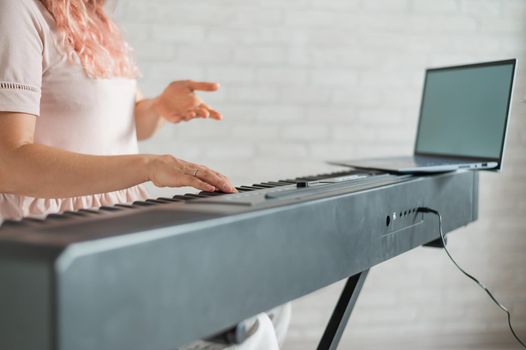 The woman plays the synthesizer and looks at the laptop screen. Close-up of female hands on the electric piano