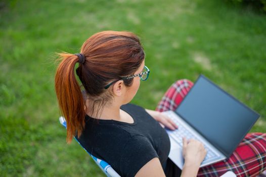 woman sits in a park and types on the computer while shopping online. The girl maintains a social distance and works outdoors on a laptop. The student is studying remotely