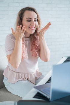 A friendly woman plays the electronic piano and conducts a video blog on her laptop. Stay home. Musical instrument teacher. Distance learning music quarantined