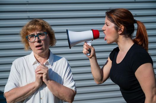 The conflict of generations. An angry middle-aged woman yells at an elderly mother through a megaphone. An adult daughter screams at an unhappy pensioner over a loudspeaker. Quarrel in the family