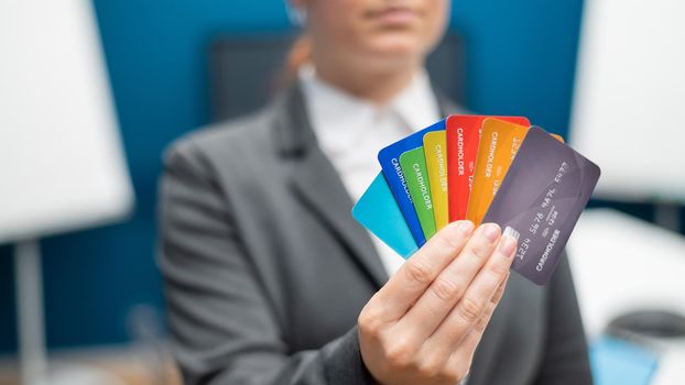 Unrecognizable woman dressed in a suit holds multi-colored plastic credit cards. A faceless bank employee offers a loan. Shopping concept. Close-up of female hands with debit cards