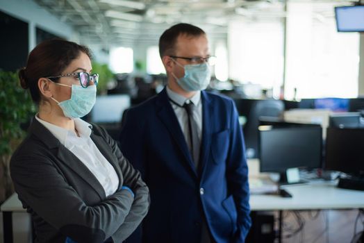 Colleagues in protective masks work in an open space office. A man and a woman in suits work at the workplace. Head and subordinate. European business people during a virus outbreak