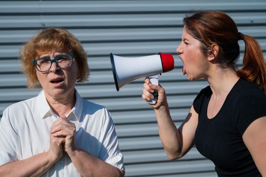 The conflict of generations. An angry middle-aged woman yells at an elderly mother through a megaphone. An adult daughter screams at an unhappy pensioner over a loudspeaker. Quarrel in the family